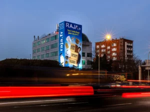Bâche publicitaire éclairée pour RAJA.fr en toiture d'immeuble sur le périphérique parisien, Porte de Clignancourt, visible de nuit avec le trafic en mouvement